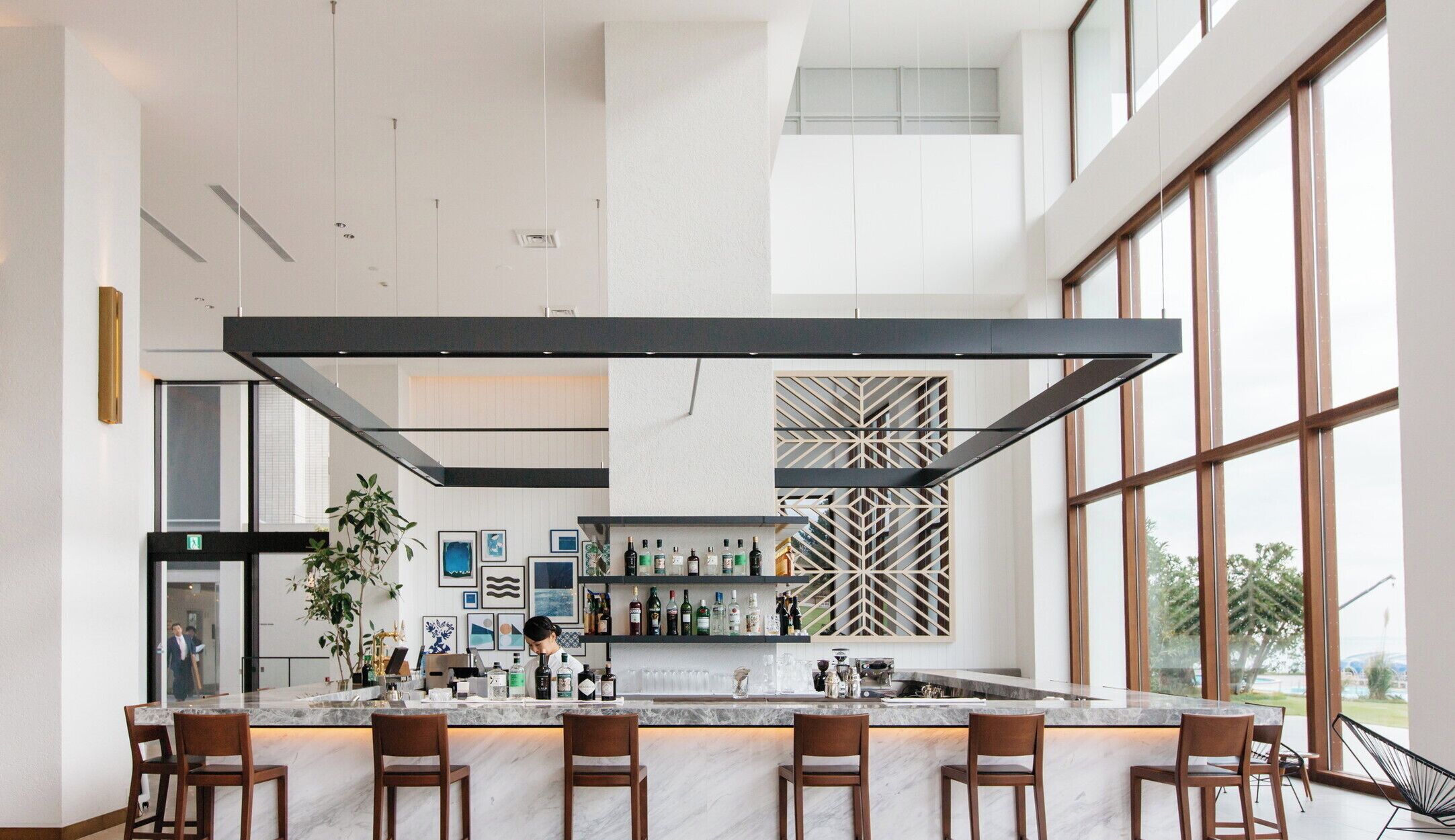 A modern bar area with a marble countertop, multiple bar stools, and a variety of bottles and glasses.