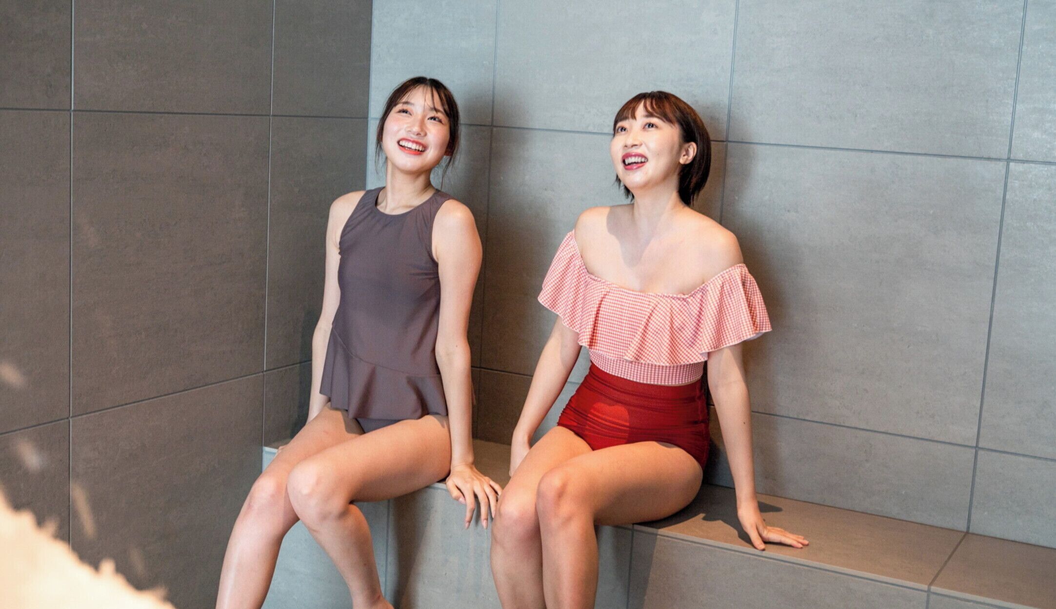 Two women sitting on a bench in a modern, tiled room.