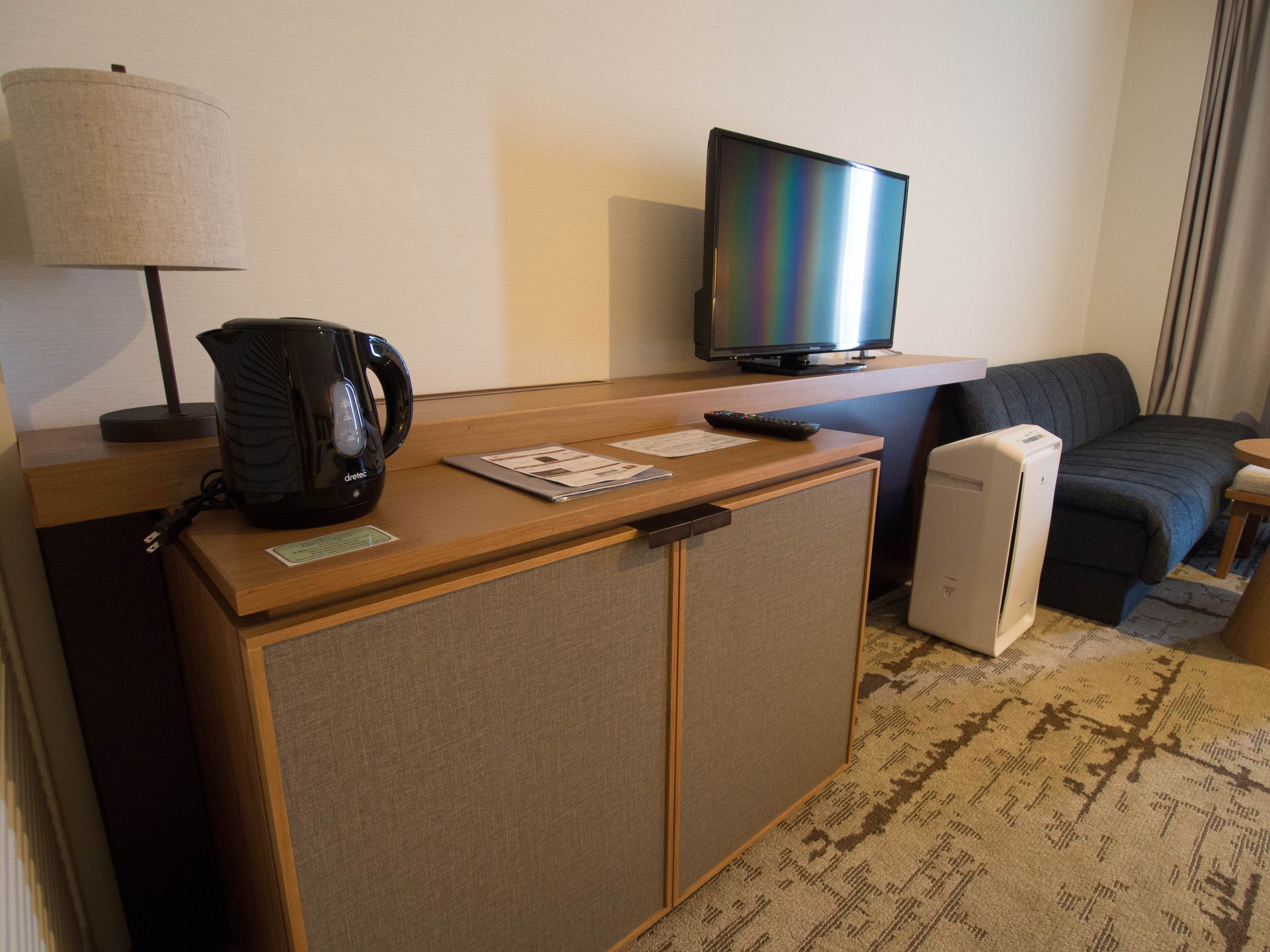 A hotel room with a wooden desk, a television, a coffee maker, a bed, and a small refrigerator.
