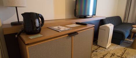 A hotel room with a wooden desk, a television, a coffee maker, a bed, and a small refrigerator.