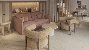 Una sala moderna con un sofá, dos sillones, una mesa de centro, un comedor con una mesa y sillas, y una escalera.