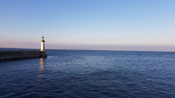 Un faro en un puerto con agua tranquila y cielo despejado.