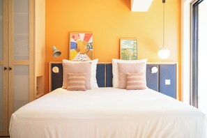 Una habitación de hotel con una cama, dos almohadas, una obra de arte en la pared, una lámpara y una ventana.