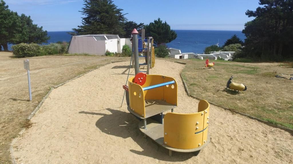 A playground with a slide and climbing structures, located near a beach with a clear view of the ocean.