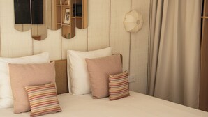 Una habitación de hotel con una cama grande, un televisor montado en la pared, un cabecero de madera y una lámpara de noche.