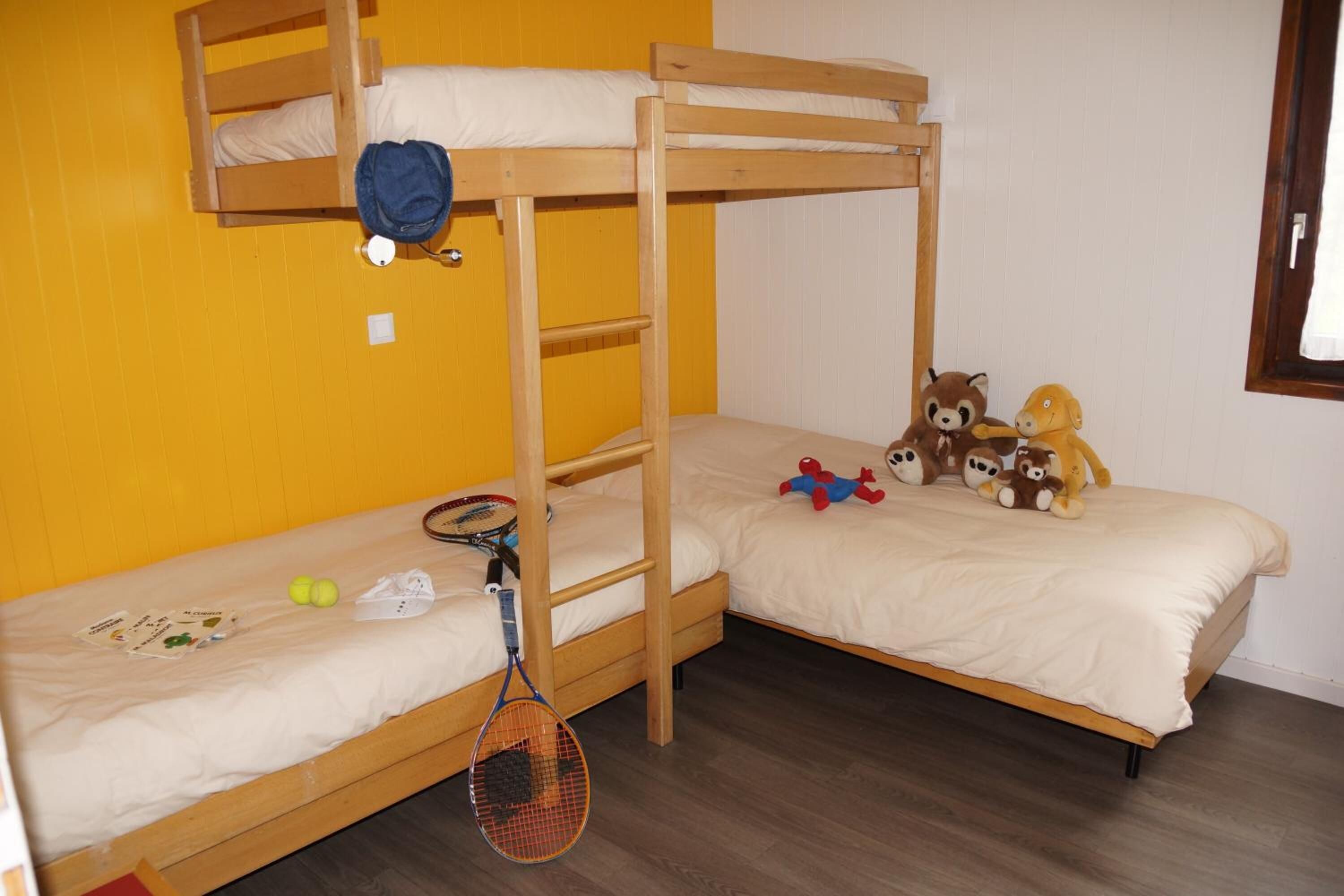 A bunk bed room with a tennis racket, balls, and stuffed toys on the beds.