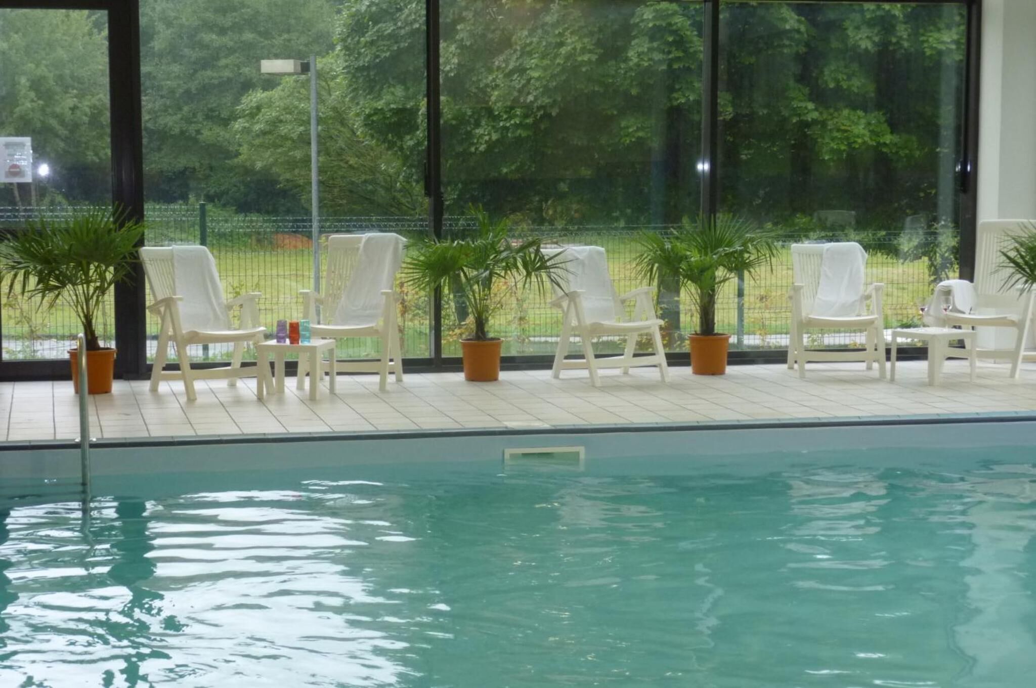 An indoor swimming pool with white lounge chairs and potted plants.