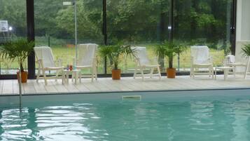 An indoor swimming pool with white lounge chairs and potted plants.