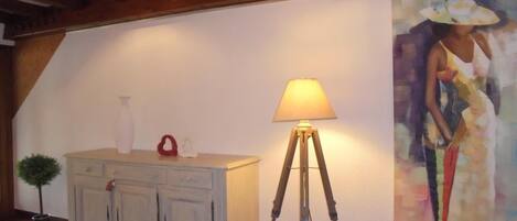 A room with a wooden ceiling, a white cabinet with decorative items, a floor lamp, and a large painting on the wall.