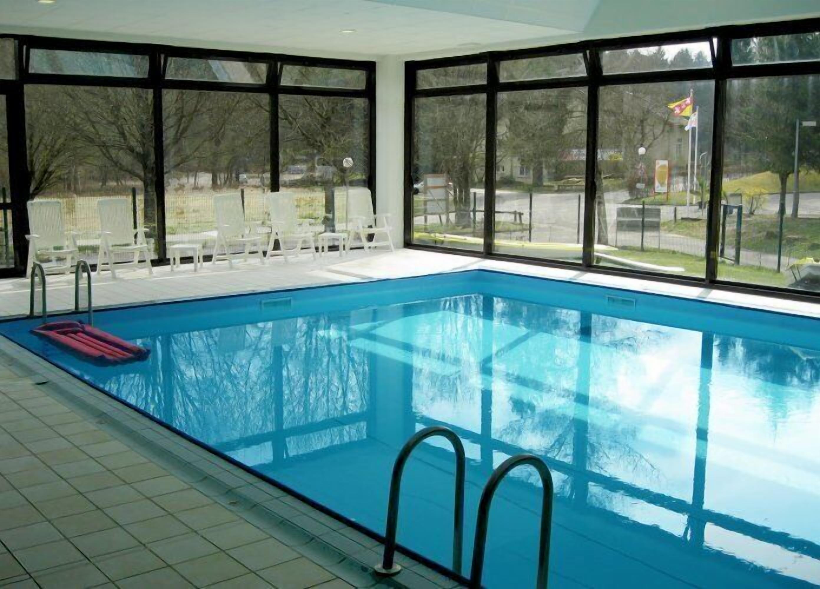 An indoor swimming pool with clear glass walls, a tiled floor, and a few lounge chairs outside.