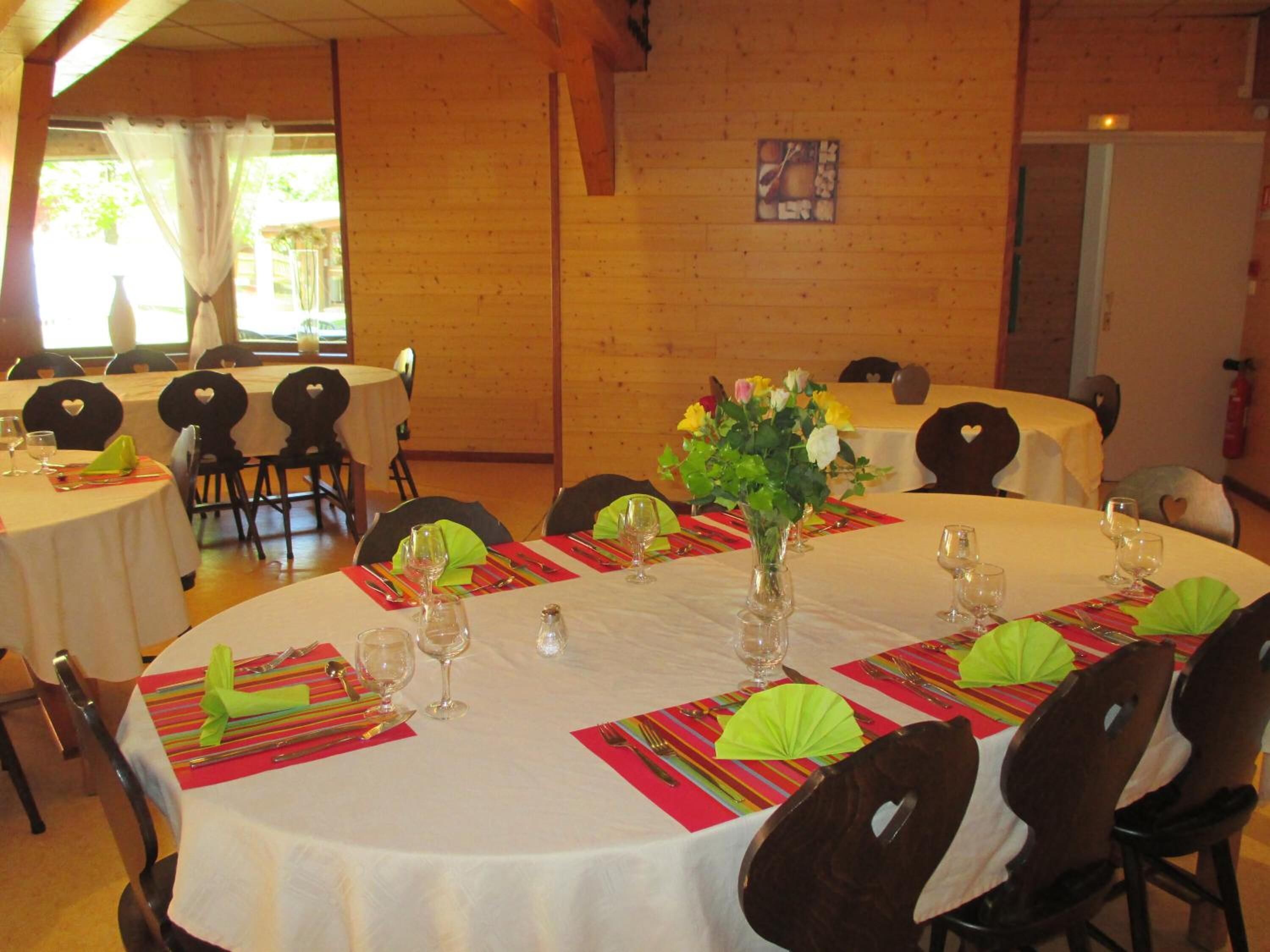 A dining area with round tables set for a meal, featuring white tablecloths, green napkins, and a vase with flowers.