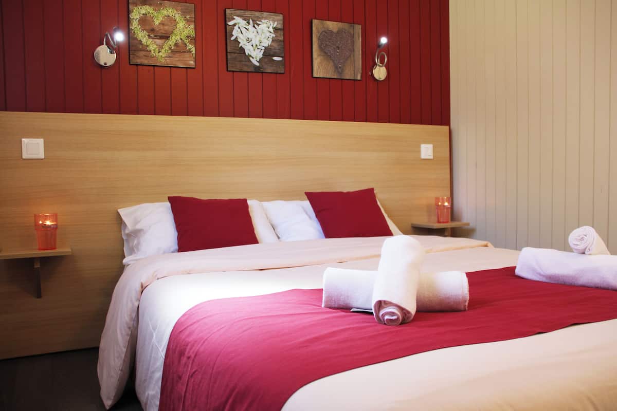 Ein Hotelzimmer mit Holz-Kopfteil, roter und weißer Bettwäsche, zwei Nachttischen mit Kerzen und einem Bild an der Wand.