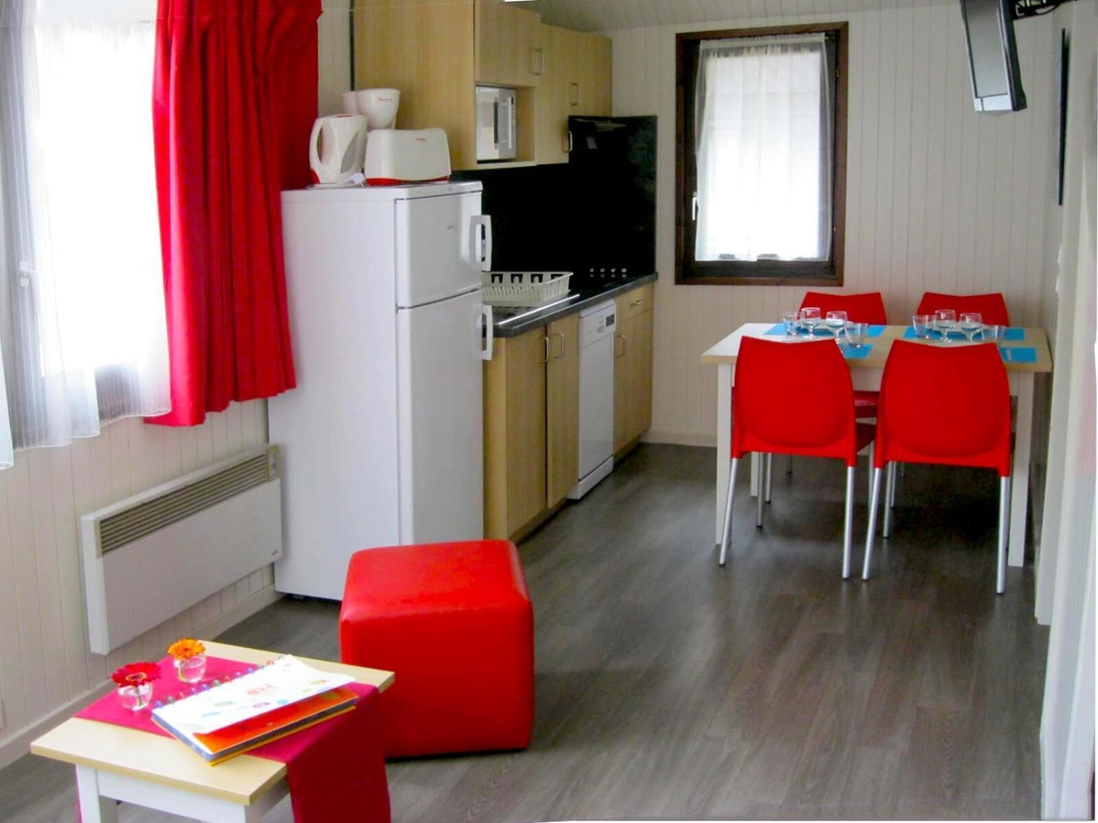 Cocina compacta con refrigerador, microondas y estufa. Zona de comedor con sillas rojas y una mesa.