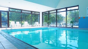 A swimming pool with clear blue water, surrounded by large windows offering views of trees and a parking area. - VVF Les Vosges Bitche (Bitche)