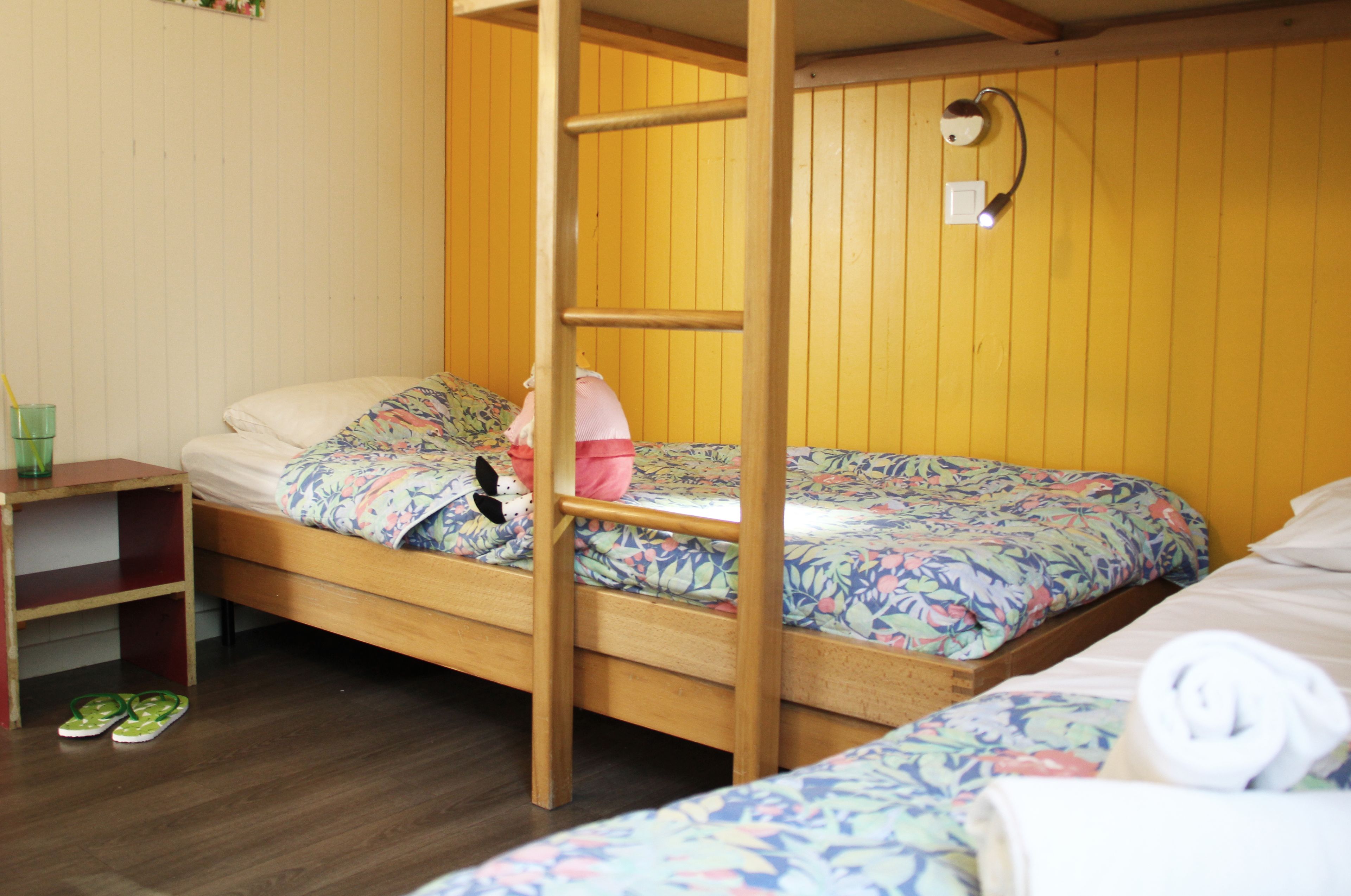 Habitación con literas, paredes de madera, una escalera, una mesita de noche y un estante.