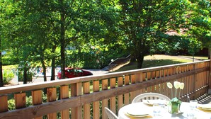 A wooden deck with a table set for dining, surrounded by white chairs, overlooking a green landscape with trees and a red car in the background. - VVF Les Vosges Bitche (Bitche)