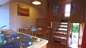 A kitchen with a stove, sink, and dining table set for four. A wooden staircase leads to an outdoor area. - VVF Les Gorges de l'Allier, Lavoûte Chilhac (Lavoute-Chilhac)