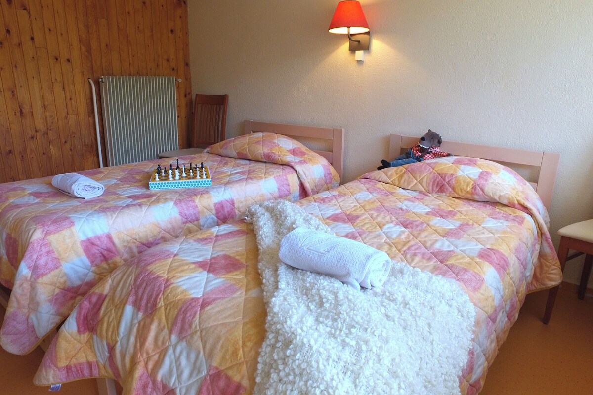 A hotel room with two beds, a chessboard, and a chair.