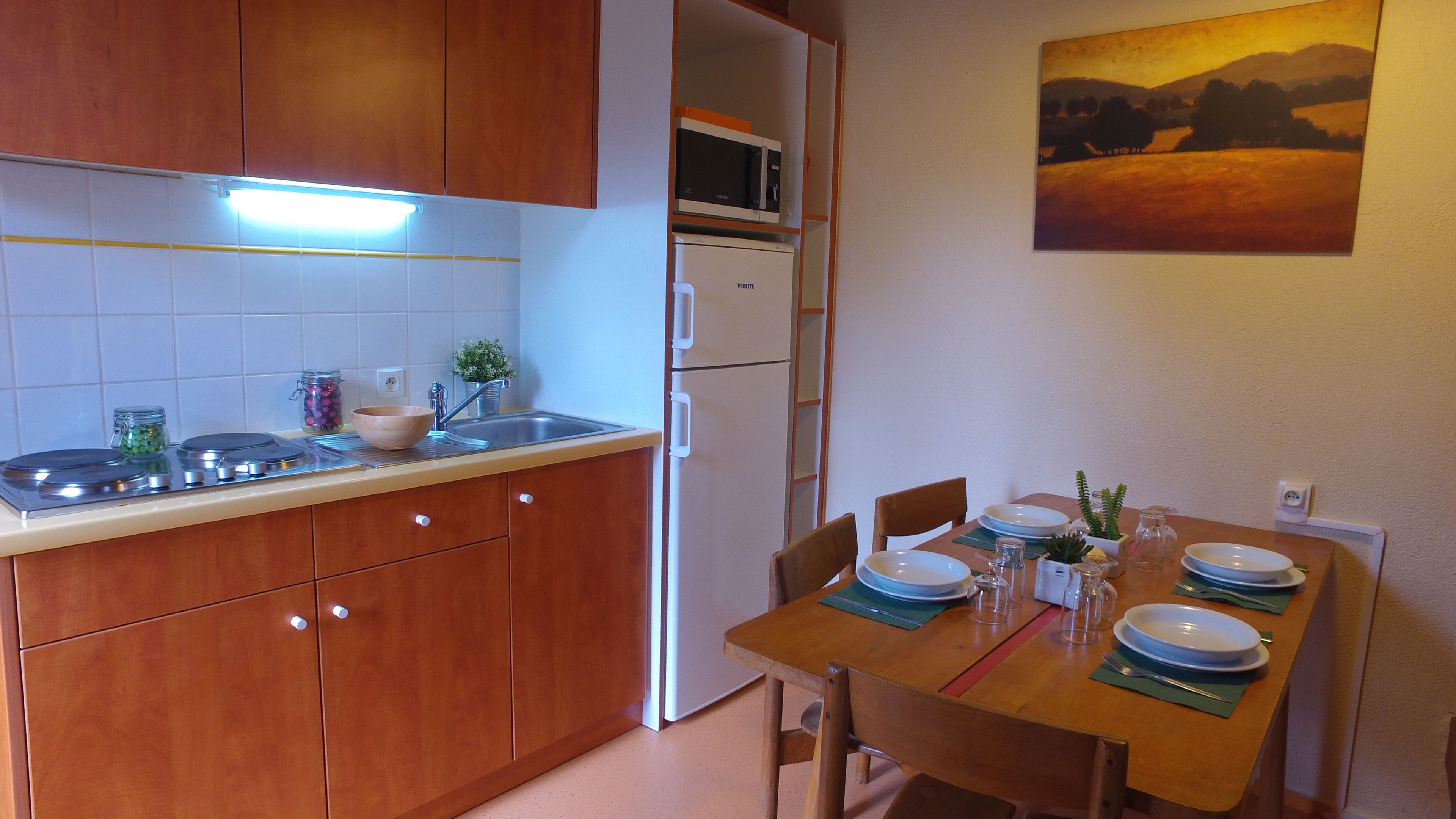 A compact kitchen with wooden cabinets, a built-in microwave, and a dining table set for four.