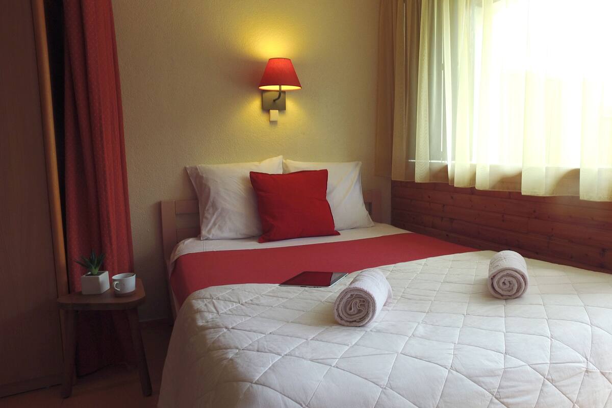 Ein Hotelzimmer mit Bett, Nachttisch, Lampe und einem Fenster mit Vorhängen.