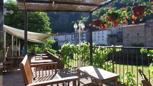 A wooden deck with tables and chairs, a pergola with a canopy, and hanging flower baskets. - VVF Les Gorges de l'Allier, Lavoûte Chilhac (Lavoute-Chilhac)