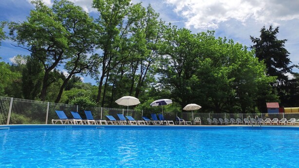A swimming pool with blue water, surrounded by a metal fence. There are lounge chairs and umbrellas along the poolside. - VVF Les Gorges de l'Allier, Lavoûte Chilhac (Lavoute-Chilhac)