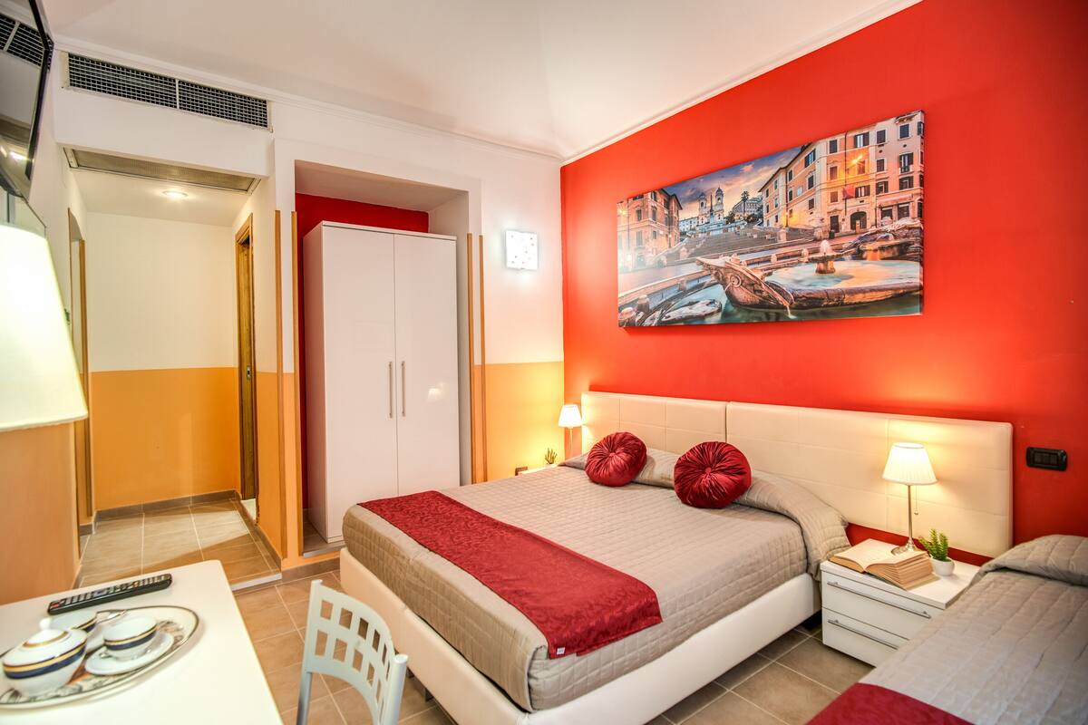Una habitación de hotel con cama, mesita de noche, lámpara y un cuadro de un paisaje urbano.