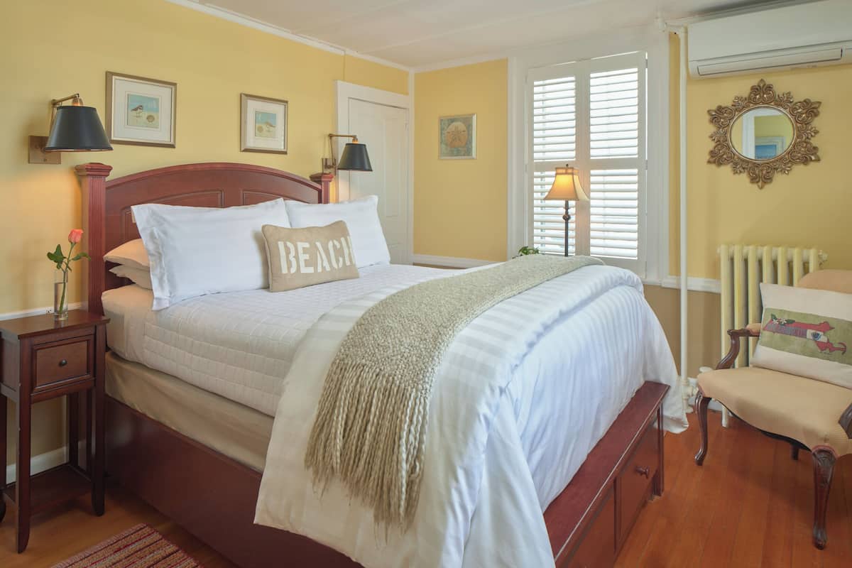 Une chambre à coucher avec un grand lit, des tables de chevet, une chaise et une fenêtre avec des stores.