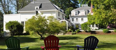 A grassy lawn with three Adirondack chairs and a house in the background.