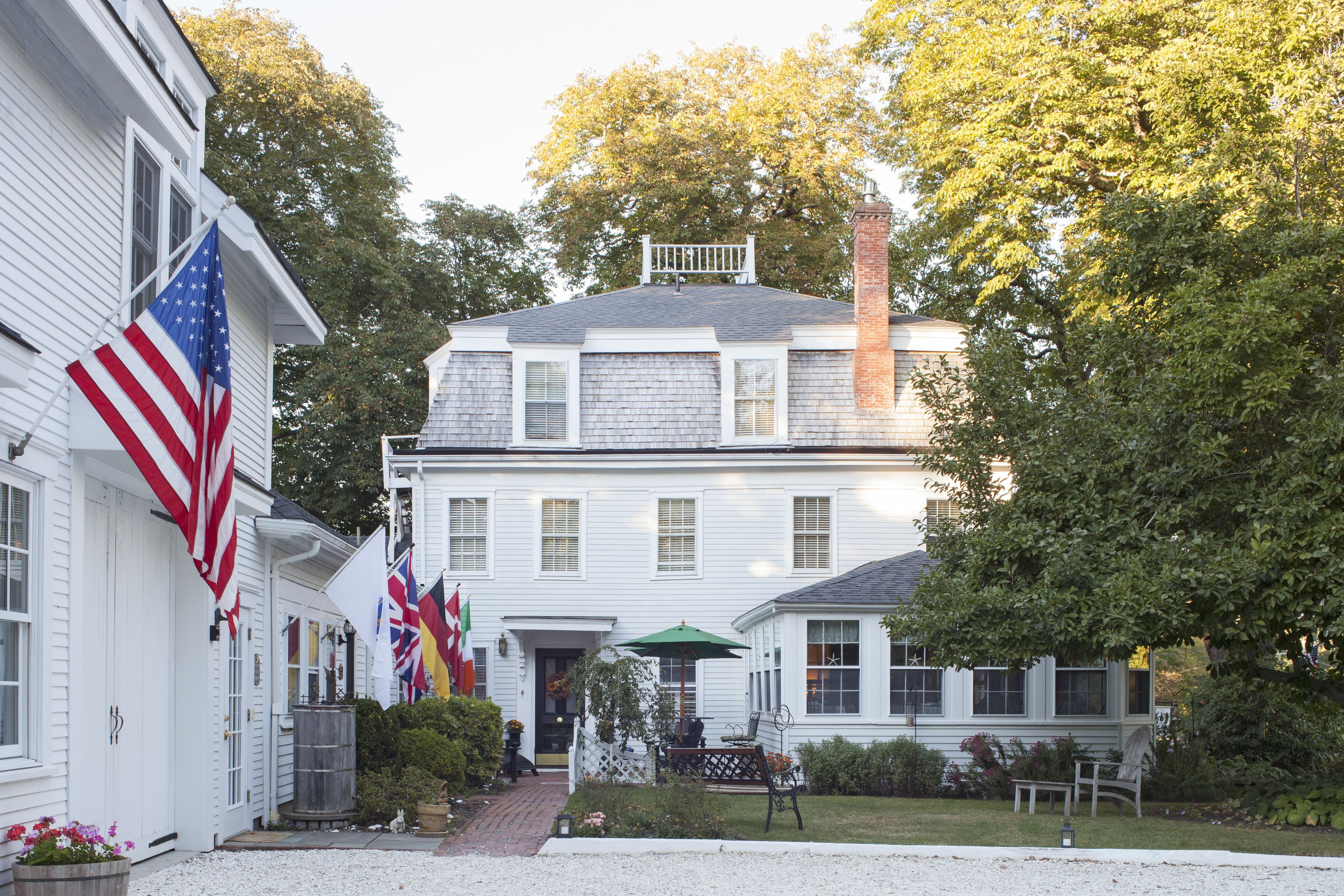 A white building with multiple flags, including the American flag, and a green umbrella in the front yard.