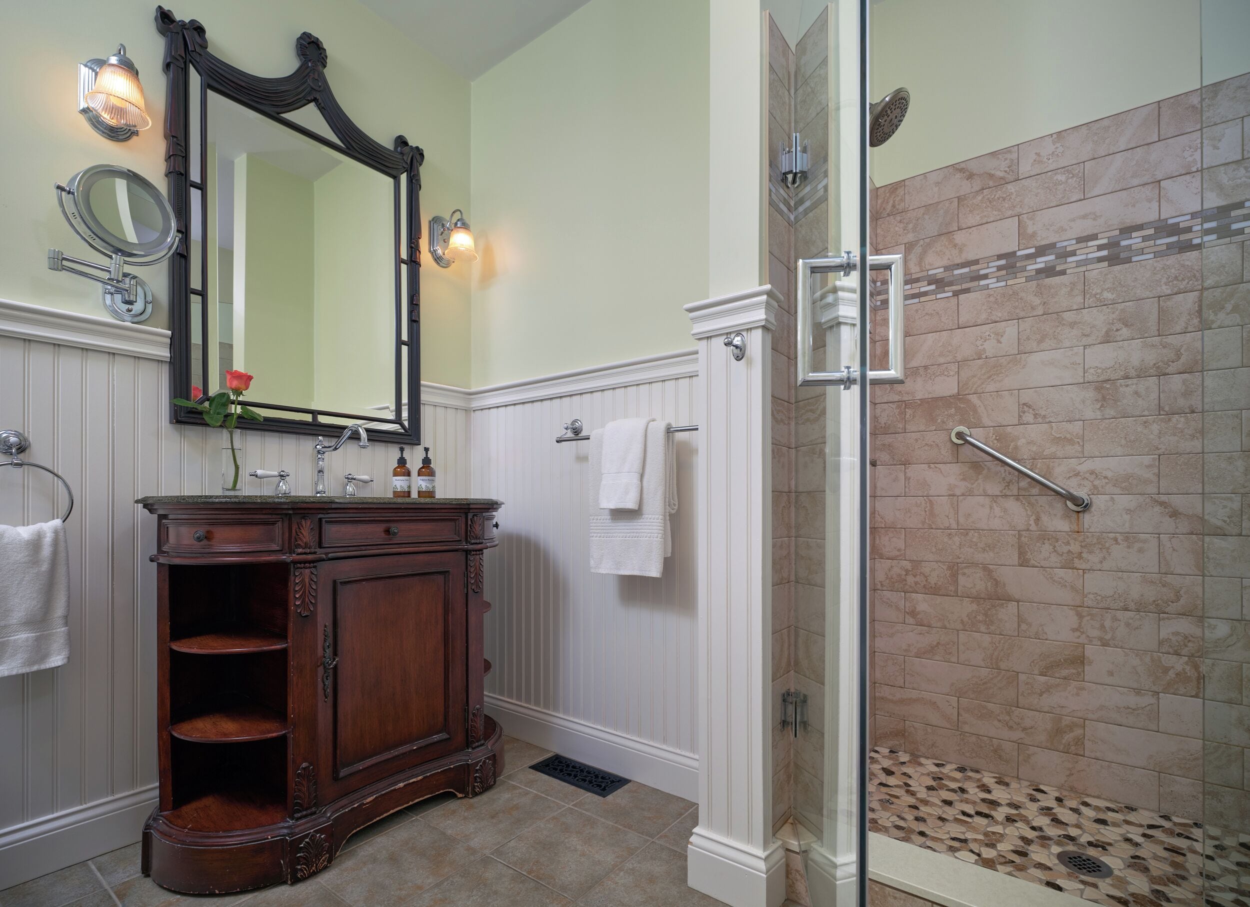 A bathroom with a vanity, a large mirror, a shower with a glass door, and a tiled shower floor.