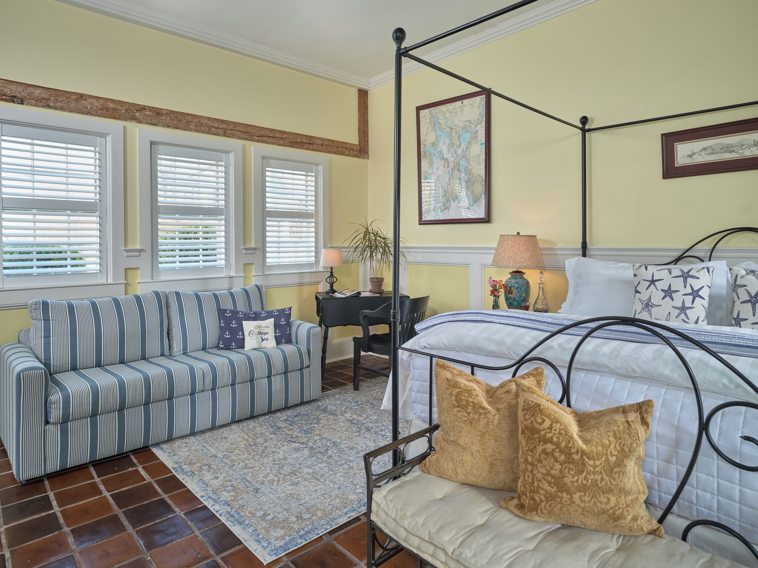 A bedroom with a four-poster bed, a striped sofa, a small desk, and a map on the wall.