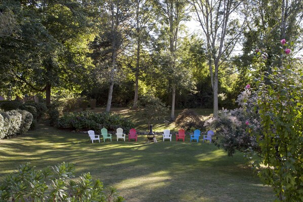 Un jardín con una fila de sillas Adirondack de colores y un pequeño hogar para fuego.