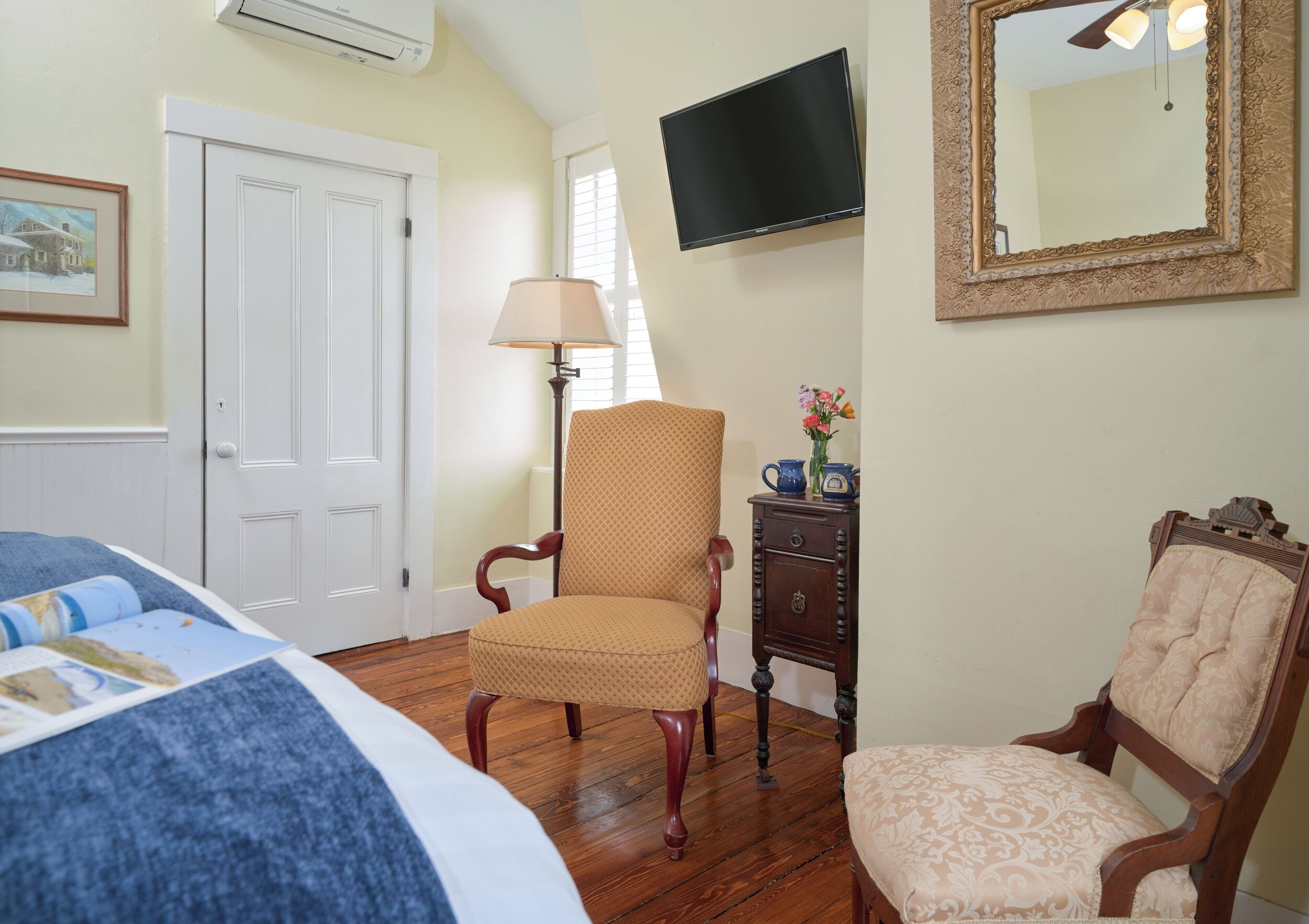 A bedroom with a bed, a chair, a dresser, a television, and a mirror.
