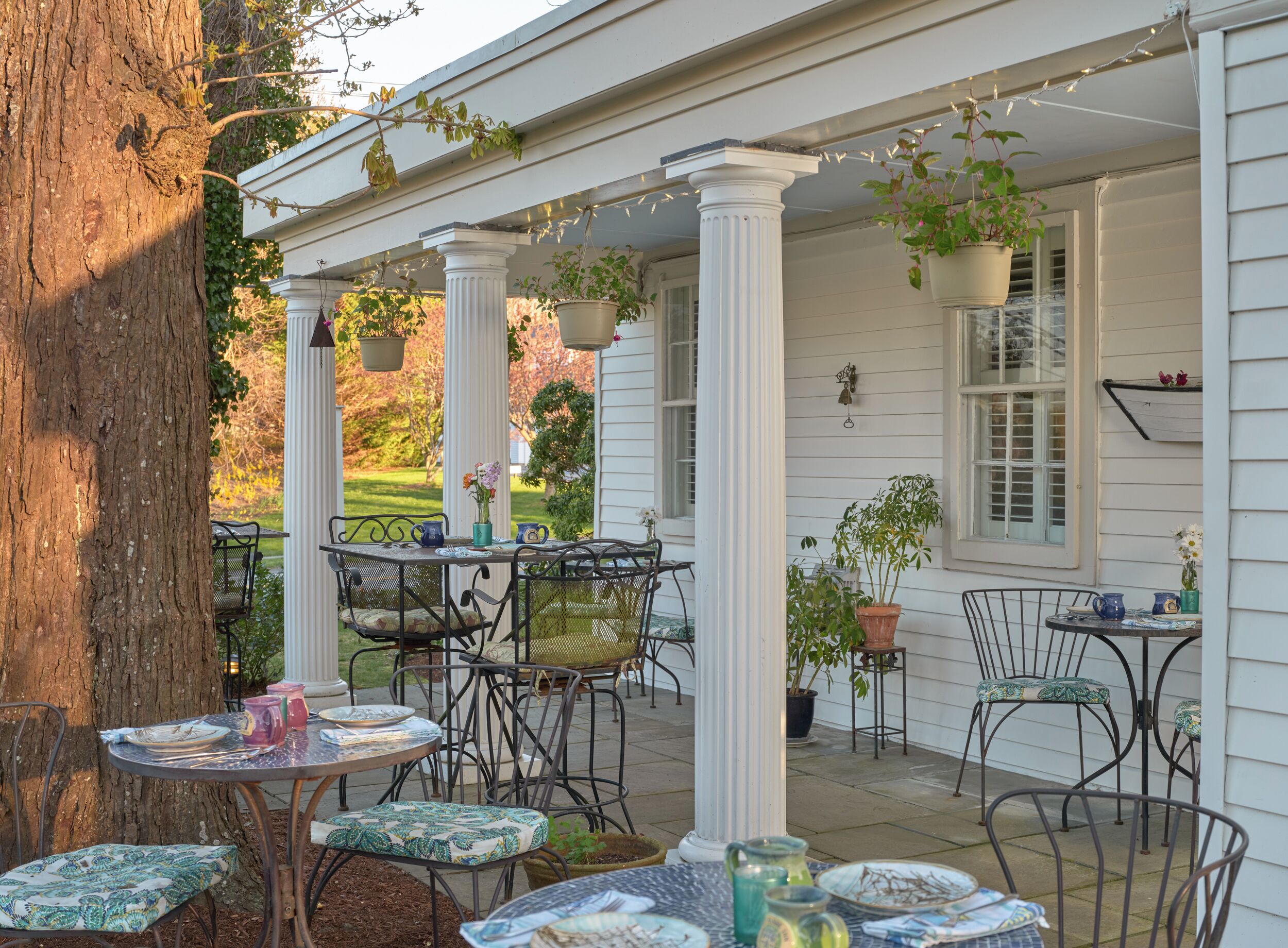 A covered patio area with outdoor seating, white columns, and hanging plants.