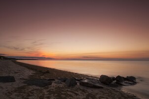 Una playa con un atardecer, agua tranquila y rocas.