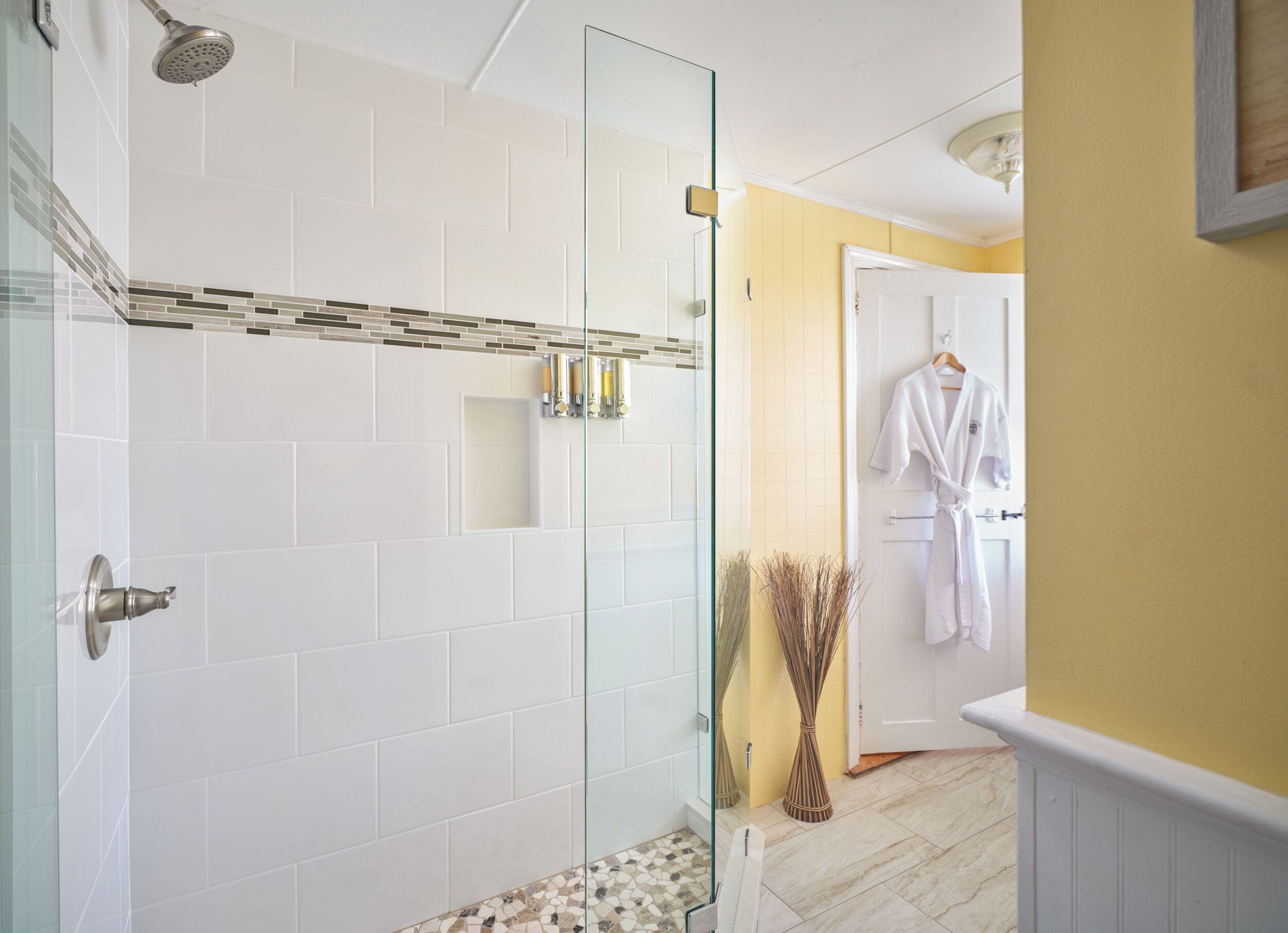 Un baño moderno con cabina de ducha de vidrio, paredes de azulejos blancos y una pared de acento amarilla.