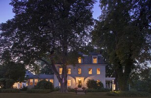 Una casa grande de dos pisos con un césped cuidado y un árbol destacado al frente.