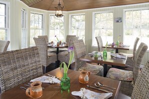 A dining area with wicker furniture, a wooden ceiling, and large windows. - The Old Manse Inn (Brewster)