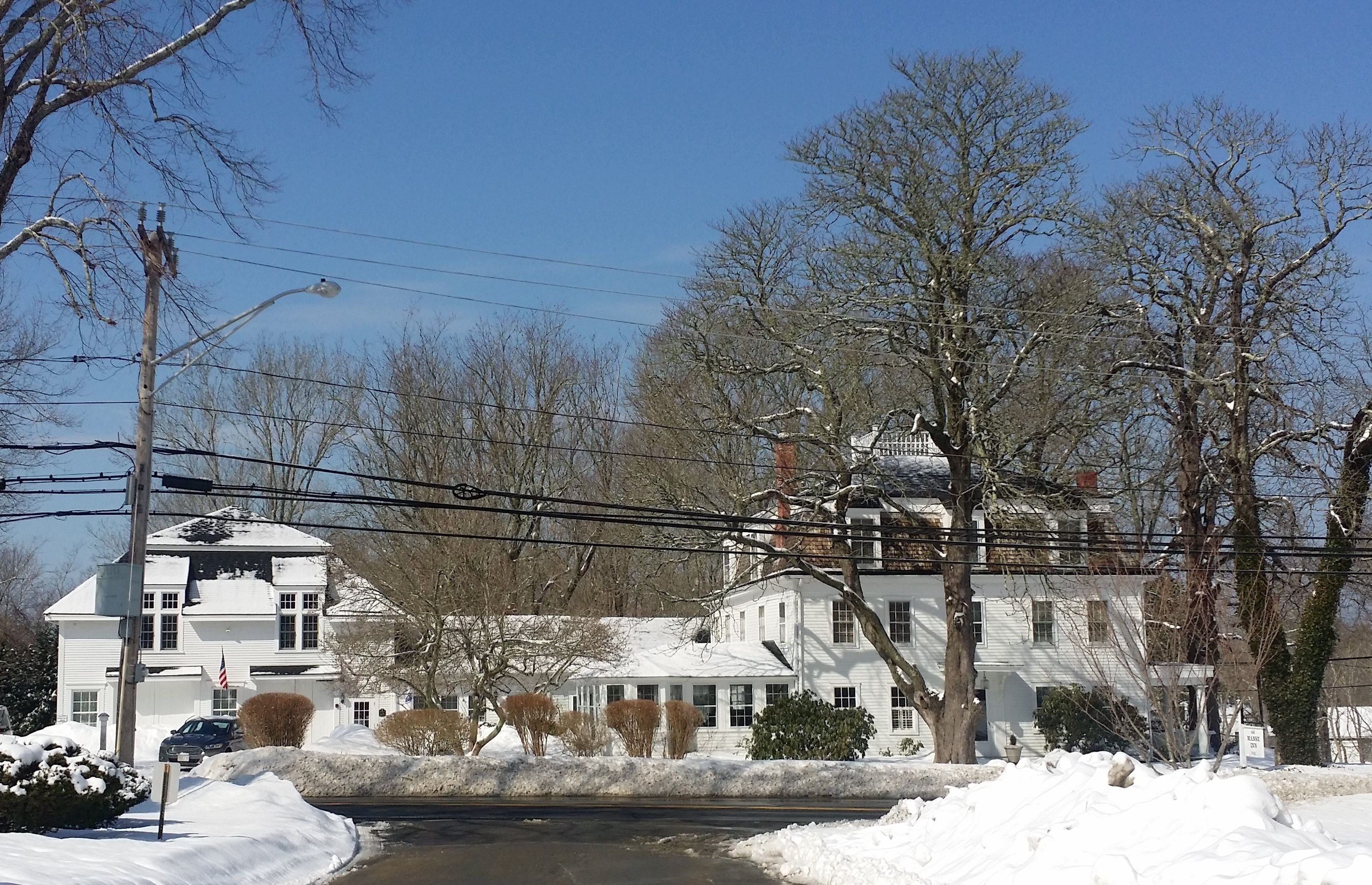 A large white house with a chimney, surrounded by snow-covered ground and leafless trees.