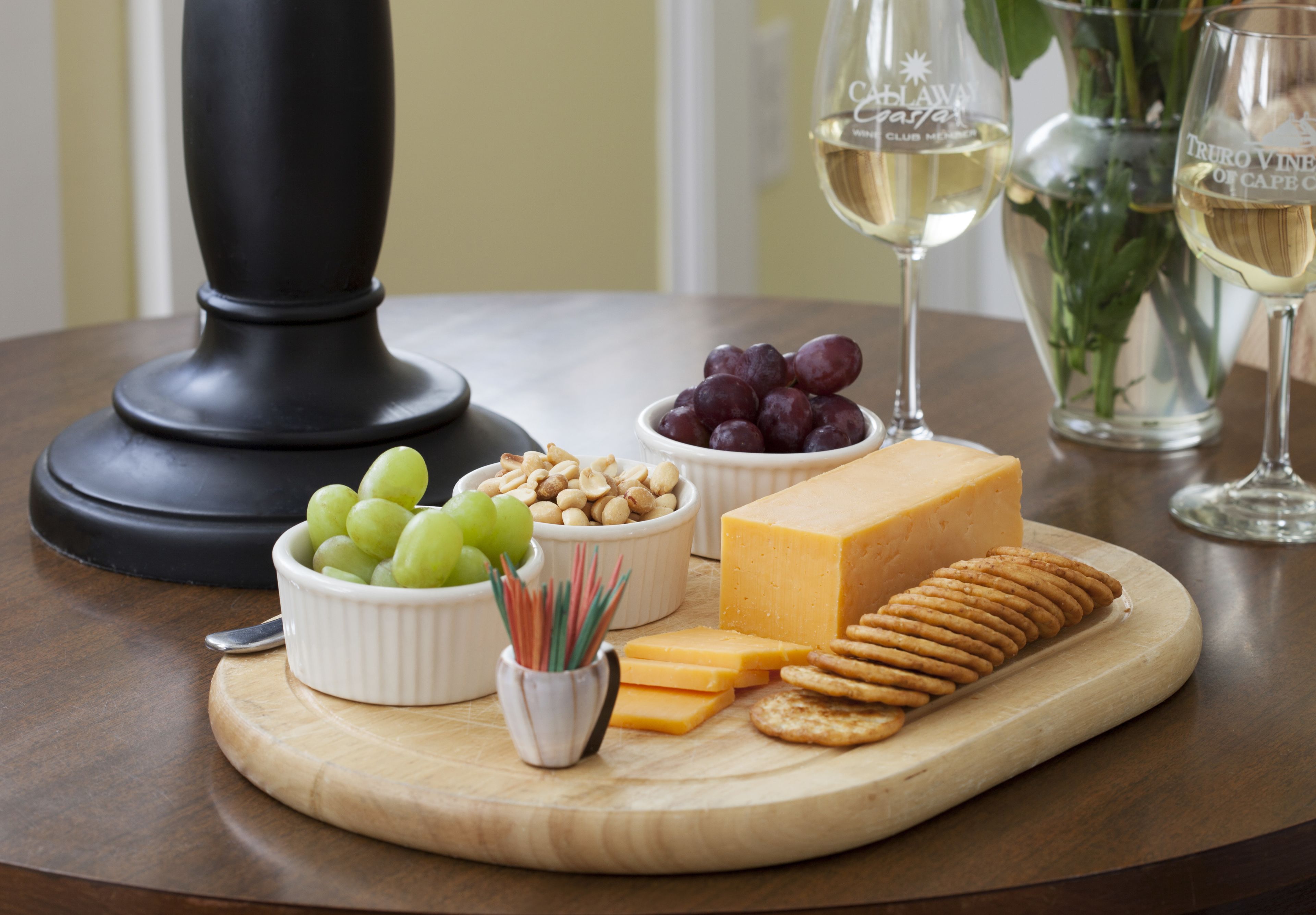 Una tabla de quesos con varios tipos de queso, galletas, uvas y nueces, todo sobre una tabla de madera.