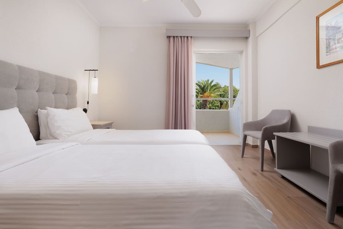 A hotel room with two beds, a desk, a chair, and a balcony with a view.