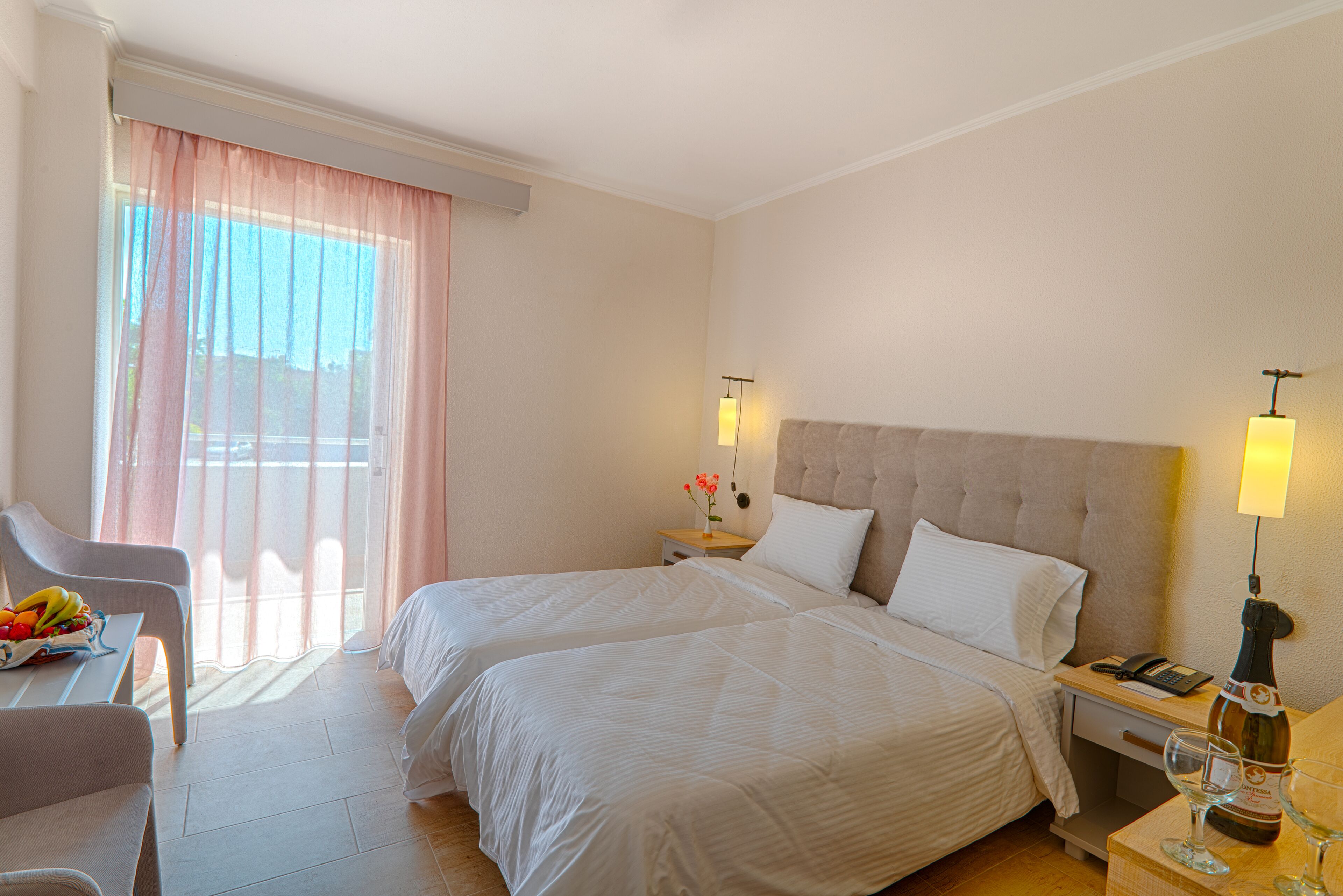 Ein Hotelzimmer mit zwei Betten, einem Schreibtisch mit Stuhl, einem Nachttisch mit Lampe und einem Fenster mit Vorhängen.