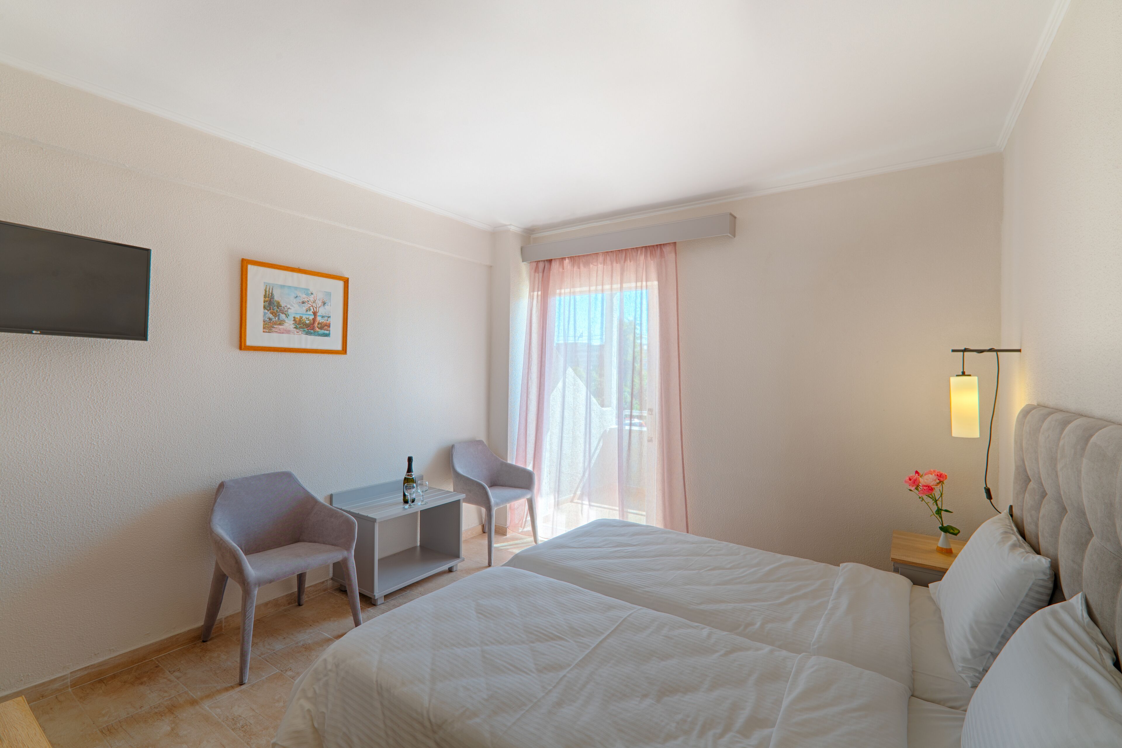 Ett hotellrum med en säng, ett skrivbord, en stol, en tv och ett fönster med gardiner.