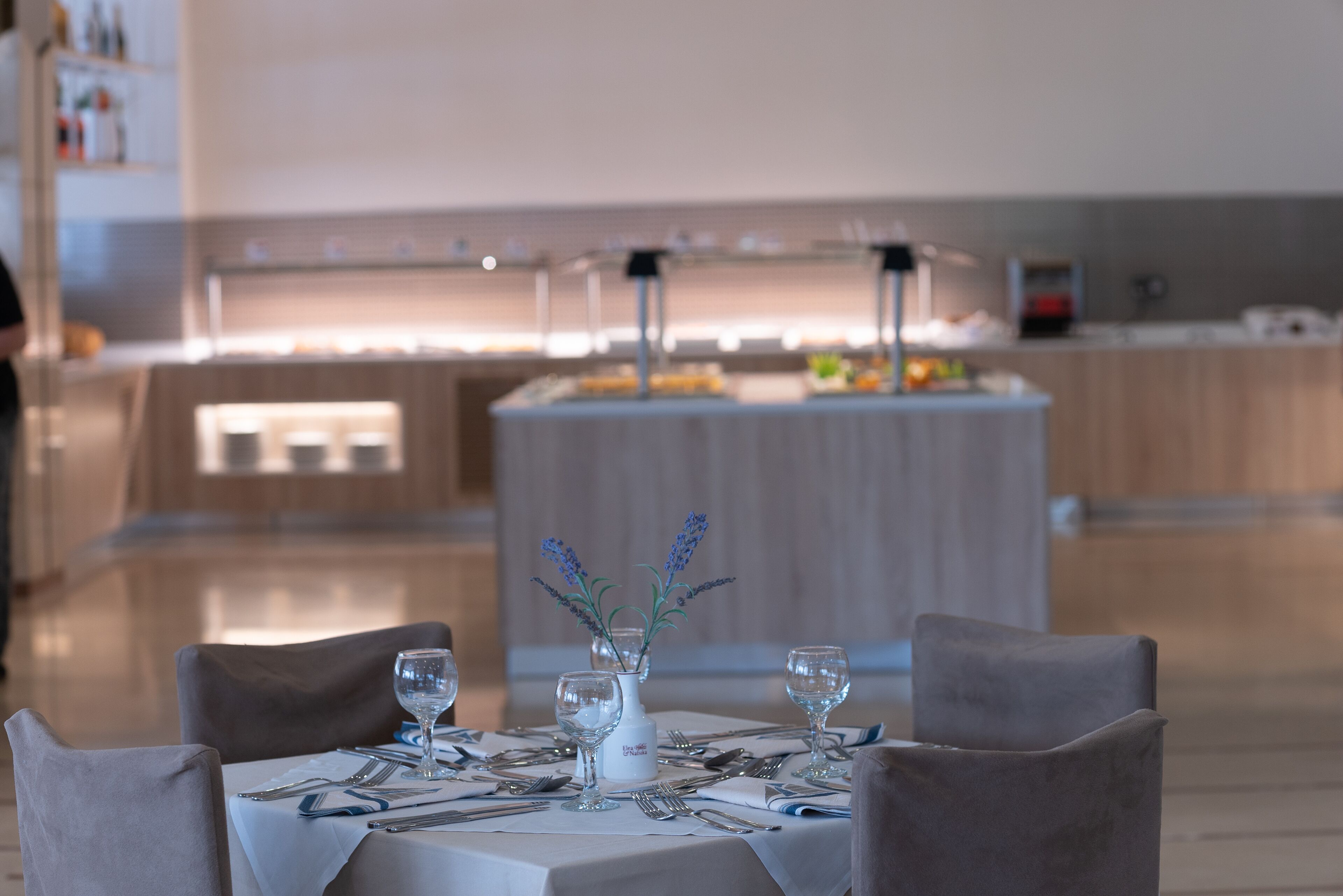 Un coin repas avec une table dressée pour quatre personnes, un vase de lavande et un buffet en arrière-plan.