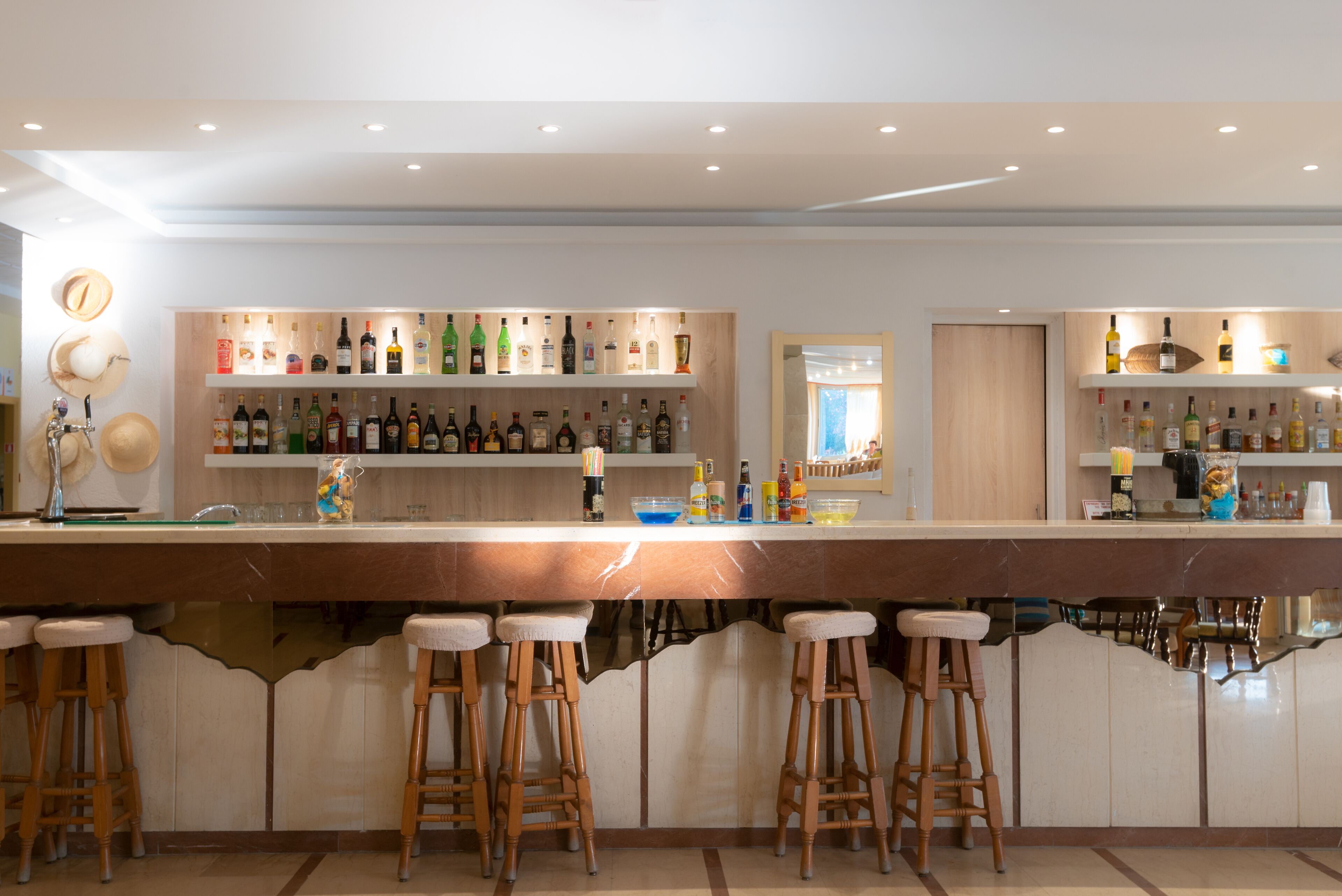 A bar area with multiple stools, shelves of bottles, and a wooden counter.