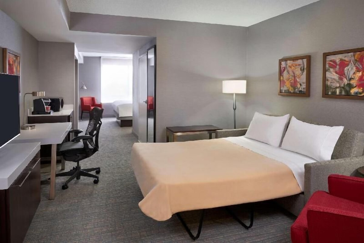 Een hotelkamer met een bed, bureau, stoel en een kleintje tafeltje.