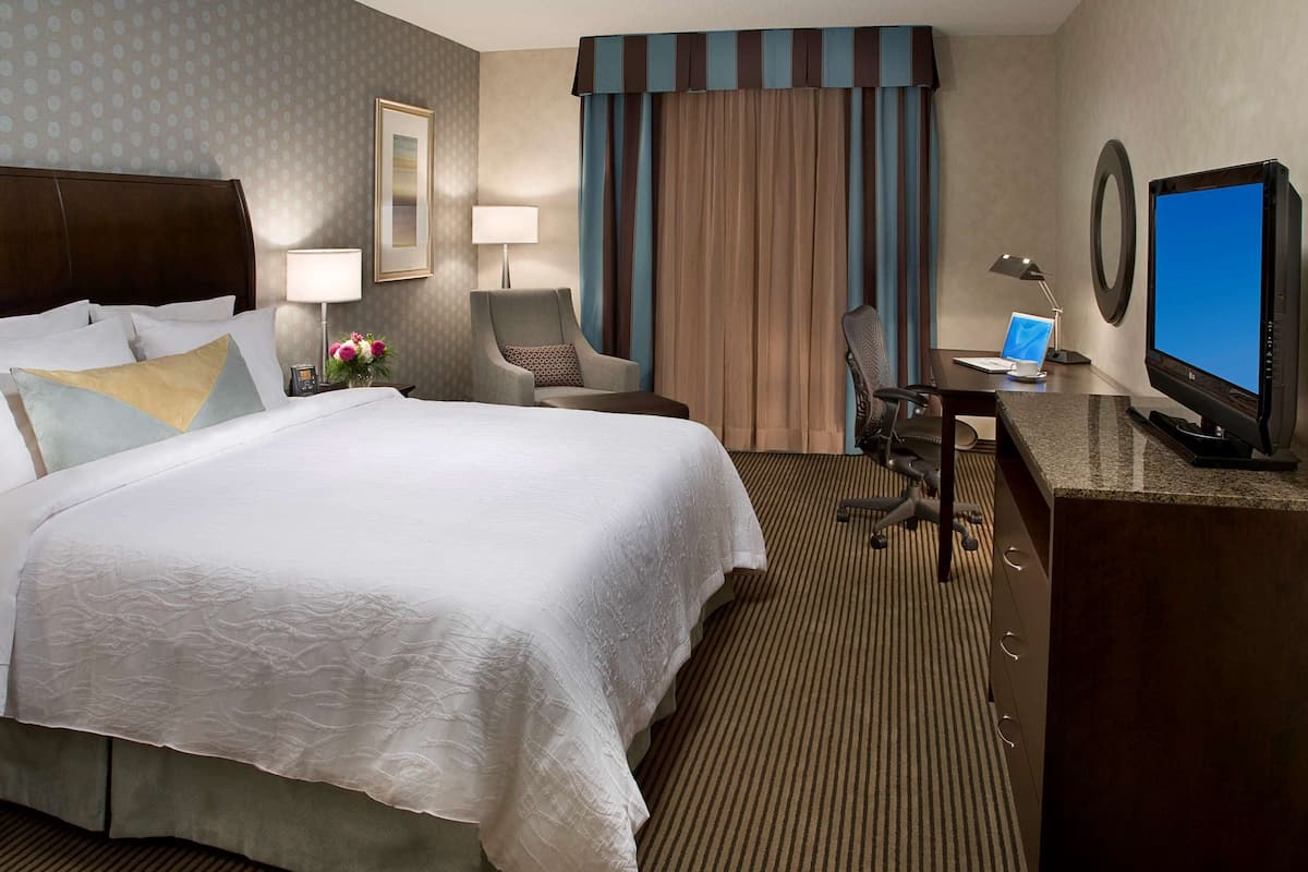 Una habitación de hotel con una cama grande, un escritorio con una computadora, una silla y un televisor.