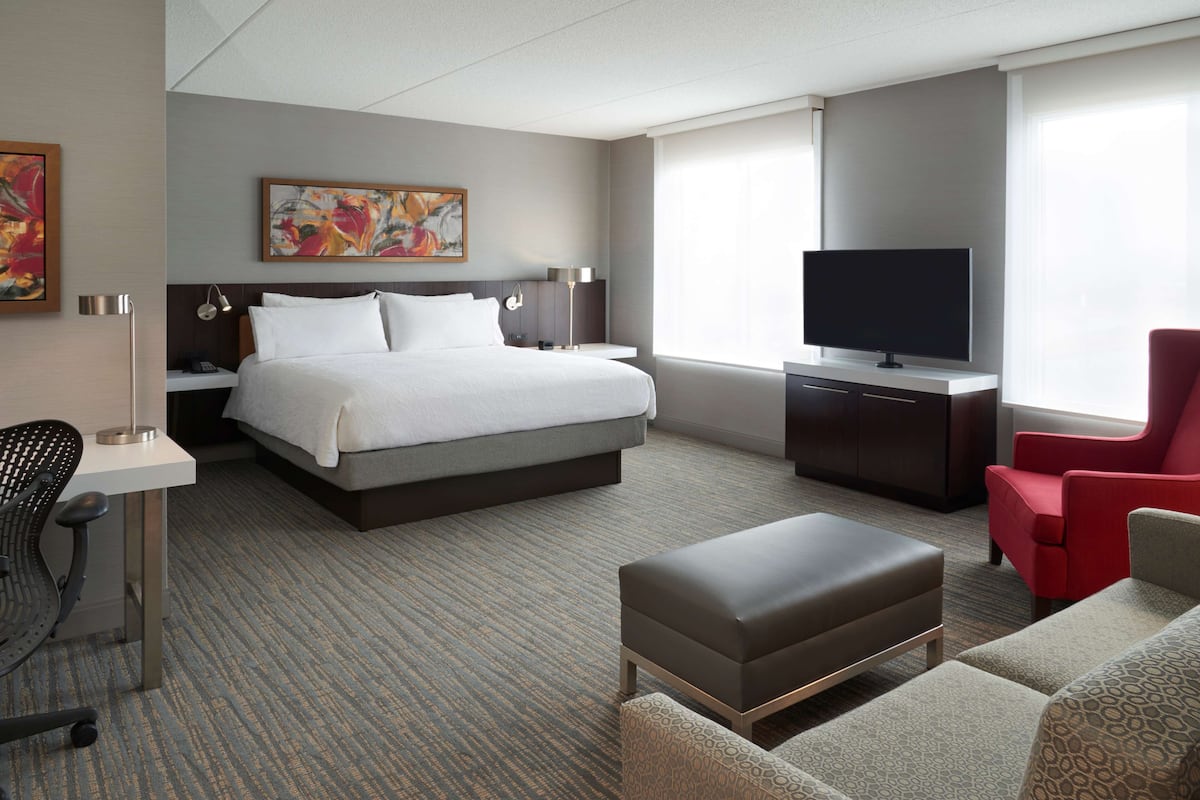 Una habitación de hotel con una cama grande, un escritorio con una silla, un televisor y un sillón rojo.