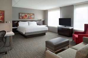Een hotelkamer met een groot bed, een bureau met stoel, een televisie en een rode fauteuil.